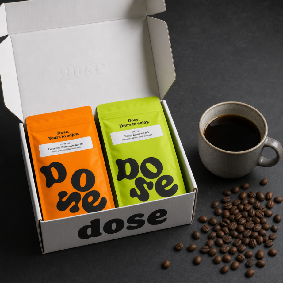 Cutia de abonament Dose Cafea de Specialitate cu 2 pungi x 250g pe fundal gri antracit cu ceasca de cafea fierbinte